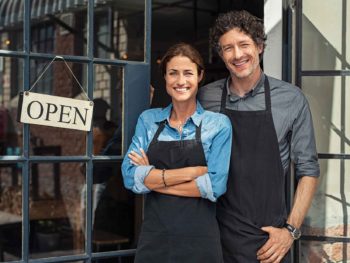 A husband and wife stand in front of their storefront needing Tax and Accounting services for their new business
