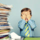 Stacks of worthless stock tax paperwork sit on a desk beside a child in button up shirt and tie holding his face in his hands in frustration.