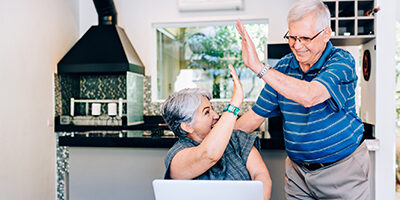 An older couple high fives each other in their home office setting as they take advantage of an low income year