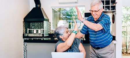 An older couple high fives each other in their home office setting as they take advantage of an low income year