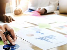 Two people sit at a desk discussing the THE DIFFERENCE BETWEEN AN AUDIT, A REVIEW, AND A COMPILATION