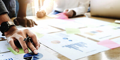 Two people sit at a desk discussing the THE DIFFERENCE BETWEEN AN AUDIT, A REVIEW, AND A COMPILATION