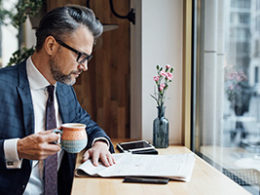 a man dressed in a business suit drinks coffee and reviews the Highlights of recent Tax law changes in a public coffee shop