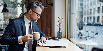 a man dressed in a business suit drinks coffee and reviews the Highlights of recent Tax law changes in a public coffee shop