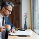 a man dressed in a business suit drinks coffee and reviews the Highlights of recent Tax law changes in a public coffee shop