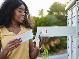 A woman stands at her mailbox holding an IRS letter wondering IRS if it's a Tax Scam Or Something You Need To Address?