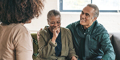 GOOD IRA NEWS FOR RETIREES, a couple sits on a couch laughing to themselves and looking happy