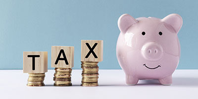 What Does A Tax Deduction Save You? T A X is spelled out in scrabble tile letters next to a small pink ceramic classic piggy bank