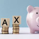 What Does A Tax Deduction Save You? T A X is spelled out in scrabble tile letters next to a small pink ceramic classic piggy bank