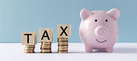 What Does A Tax Deduction Save You? T A X is spelled out in scrabble tile letters next to a small pink ceramic classic piggy bank