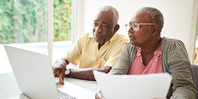 Running Low on Money? Congress Has Made It Easier for You to Tap Your Retirement Savings. A couple sits in front of a laptop smiling