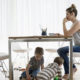 Working from Home During The COVID-19 Outbreak. a woman sits at a kitchen table working on a laptop with two little ones playing underneath her.