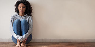 How Can I File for Unemployment in The United States? A woman sits on the floor, back against the wall, alone.