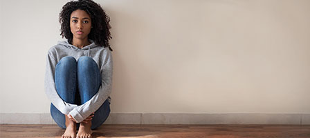 How Can I File for Unemployment in The United States? A woman sits on the floor, back against the wall, alone.