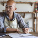 Video: Self-Employed Individuals Now Qualify For Unemployment. A tradesman works on a laptop in his workshop wearing a shop apron