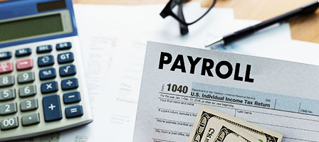 Employers Can Defer Payroll Taxes, show a calculator, PAYROLL sheet and a pair of glasses sitting on a desk.