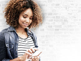 The IRS Provides Online Tools for Recovery Rebates, a woman stands against a wall, checking her phone with a smile