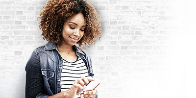 The IRS Provides Online Tools for Recovery Rebates, a woman stands against a wall, checking her phone with a smile