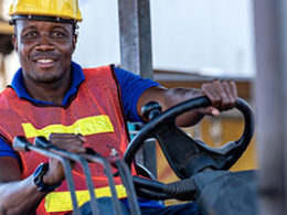 What the Employee Retention Credit Means to You. A blue collar worker runs a forklift, both hands on the controls.