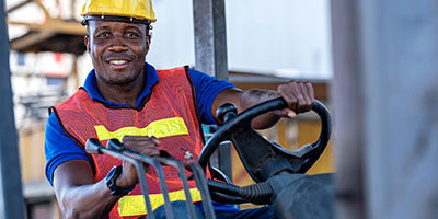 What the Employee Retention Credit Means to You. A blue collar worker runs a forklift, both hands on the controls.