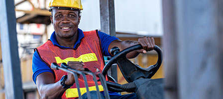 What the Employee Retention Credit Means to You. A blue collar worker runs a forklift, both hands on the controls.