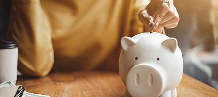 2020 RMD Rollover Relief - A hand puts a penny in a pale pink ceramic piggy bank