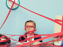 Government Keeping Your Refund? A child dressed in a suit sits at a desk completely surrounded and covered in red tape