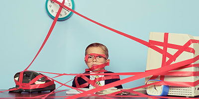 Government Keeping Your Refund? A child dressed in a suit sits at a desk completely surrounded and covered in red tape