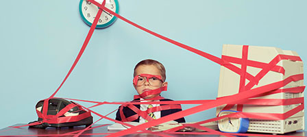 Government Keeping Your Refund? A child dressed in a suit sits at a desk completely surrounded and covered in red tape