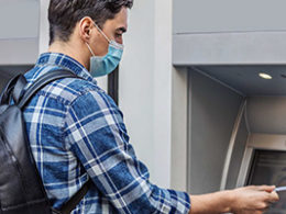 Do You Know Unemployment Benefits Are Taxable? A young man approaches a cash machine wearing a mask due to COVID.