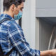 Do You Know Unemployment Benefits Are Taxable? A young man approaches a cash machine wearing a mask due to COVID.