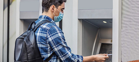 Do You Know Unemployment Benefits Are Taxable? A young man approaches a cash machine wearing a mask due to COVID.