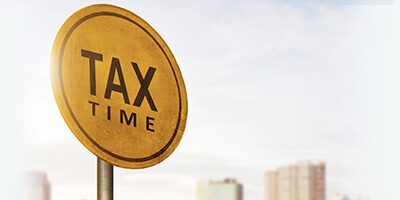 October's Extended Due Date is Almost Here. Scott Nissen at Nissen and Associates can help you with your taxes. A round sign proclaiming Tax Time on a metal pole with a blurred cityscape background