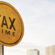 October's Extended Due Date is Almost Here. Scott Nissen at Nissen and Associates can help you with your taxes. A round sign proclaiming Tax Time on a metal pole with a blurred cityscape background