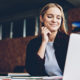 Actually, A Recession Is A Great Time to Launch That New Startup says a woman smiling proudly at her laptop, dressed in business casual clothes.