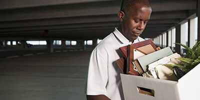 Tax Consequences of Losing Your Job, a sad faced person walks away with a box full of personal effects in a car garage.