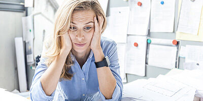 What Happens If I Missed the October 15th Tax Extension Deadline? A woman with tax problems sits holding her head in her hands with an overwhelmed expression on her face.