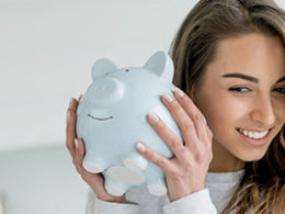 Saver's Credit Can Help You Save For Retirement, a woman holds up a piggy bank to her ear.