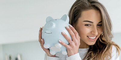 Saver's Credit Can Help You Save For Retirement, a woman holds up a piggy bank to her ear.