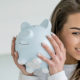 Saver's Credit Can Help You Save For Retirement, a woman holds up a piggy bank to her ear.