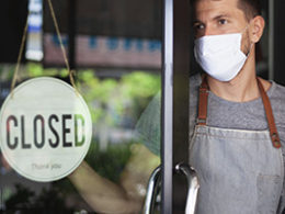 New COVID Relief Law passed in 2020. A man in a mask stands inside his shop, turning the open sign to closed.