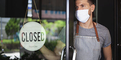 New COVID Relief Law passed in 2020. A man in a mask stands inside his shop, turning the open sign to closed.