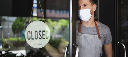 New COVID Relief Law passed in 2020. A man in a mask stands inside his shop, turning the open sign to closed.