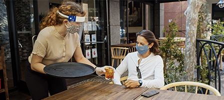 Congress Has Authorized a Second Round of PPP Loans, A server wearing a mask passes a drink to a customer on a restaurant patio.