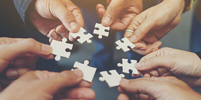 What Is A Joint Venture? Four hands come together holding puzzle pieces