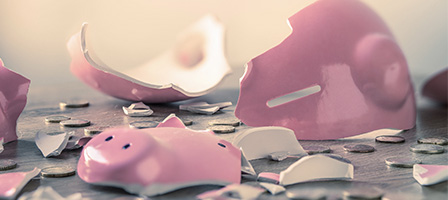 Unemployment Fraudsters May Create A Tax Nightmare for Unsuspecting Taxpayers, A broken piggy bank lies smashed on a table with a few coins scattered about.