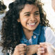 Are You Missing Out On The Increased Child Tax Credit? A young girl with curly black hair smiles at an adult.