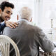 2023 Social Security Cost Of Living Increase Highest In 40 Years A young man puts his arm around an older man while they sit together at a cozy kitchen table.