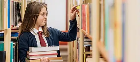 Understanding the Kiddie Tax: a youth holding a stack a books walks down a library aisle reading titles.