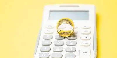 Video Tips: Love & Taxes: Essential Tips For Tax Planning Before You Get Married. A gold wedding ring sits on top of a calculator.